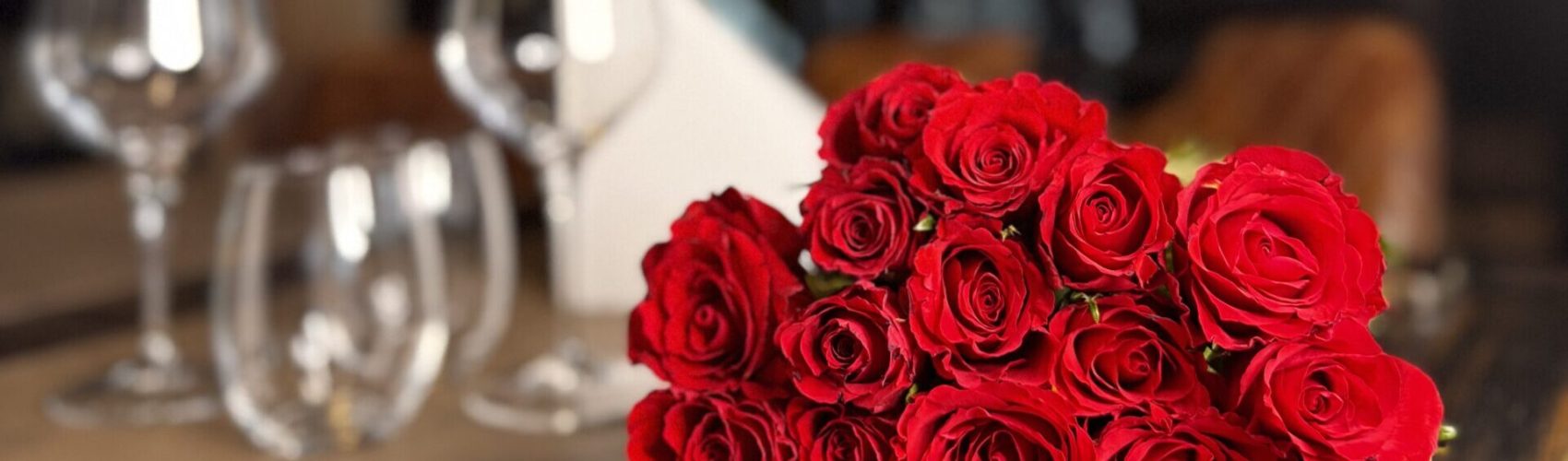 Punainen ruusukimppu Ravintola Obelix Riihimäen pöydällä, taustalla viinilaseja ja valkoinen lautasliina, luoden elegantin ja romanttisen tunnelman. Red rose bouquet on a table at Restaurant Obelix in Riihimäki, with wine glasses and a folded white napkin creating an elegant, romantic atmosphere.