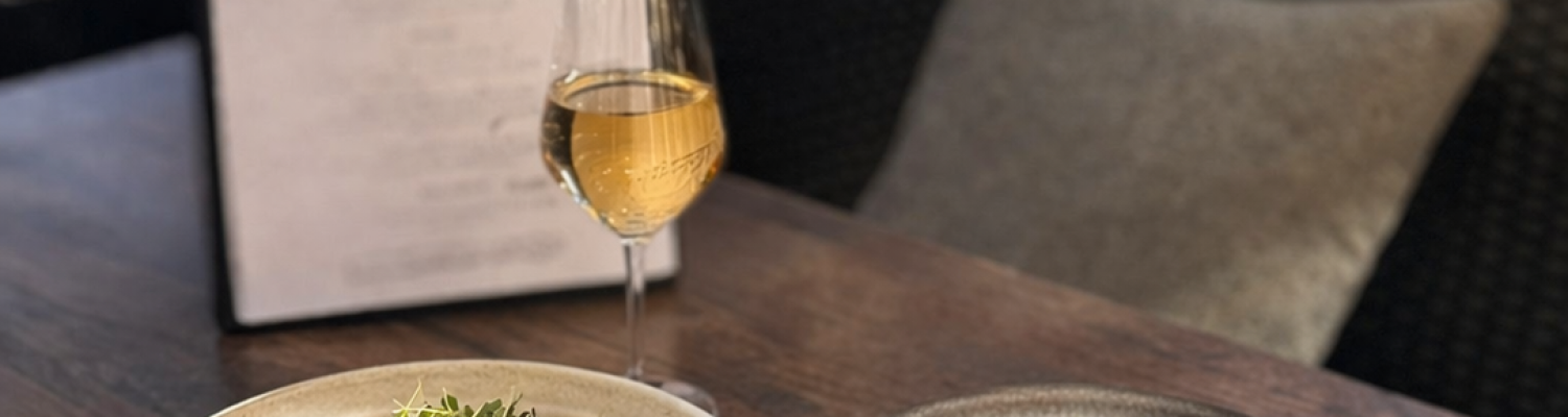 Kaksi kauniisti aseteltua ravintola-annosta ja valkoviinilasi pöydällä; kuva Ravintola Obelix Riihimäen laadukkaasta ruokailu- ja makuelämyksestä. Two elegantly plated restaurant dishes and a glass of white wine on the table; image showcasing the dining experience at Restaurant Obelix Riihimäki.